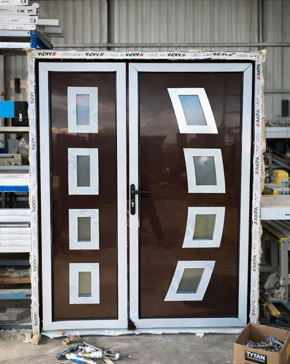 Dvokrilna PVC ulazna vrata sa dekorativnim staklenim panelima u fazi izrade u radionici, vidljiva zaštitna traka i montažni materijal