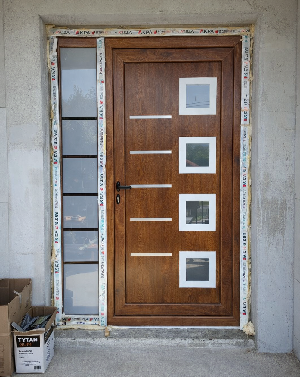Ulazna vrata u drvo dekoru sa bočnim svetlom u fazi montaže, vidljiva pur pena i zaštitne trake oko rama